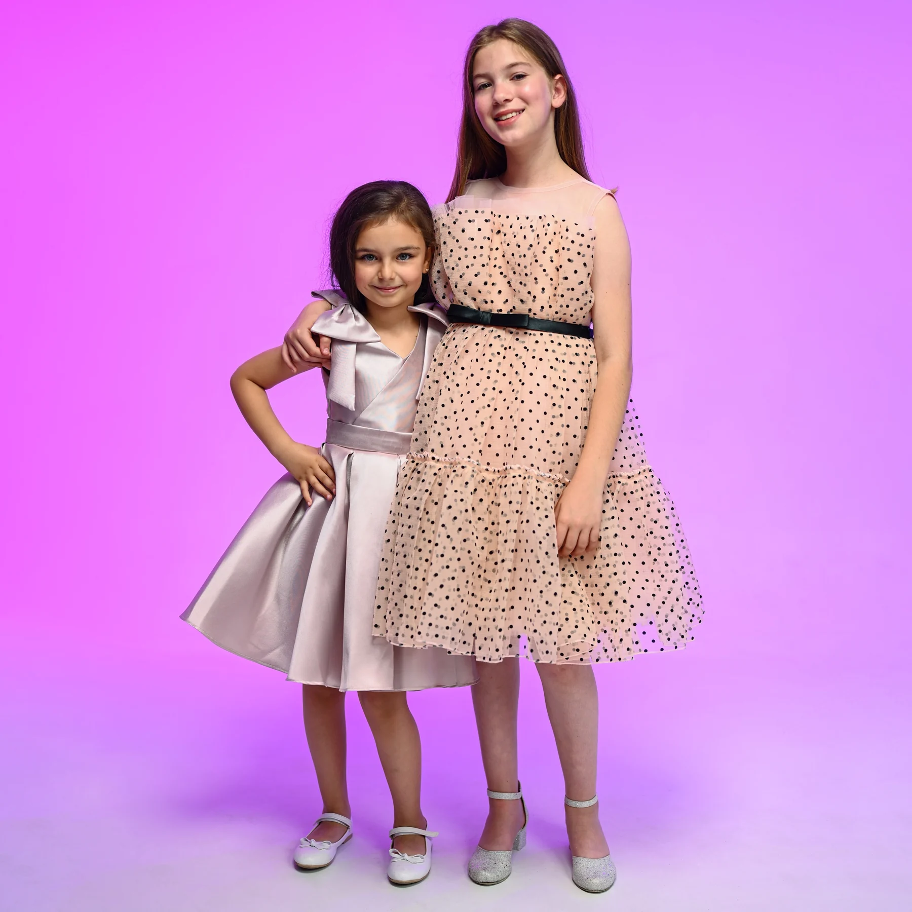 Pembe fonda farklı elbiseleri yan yana gösteren iki çocuk model.